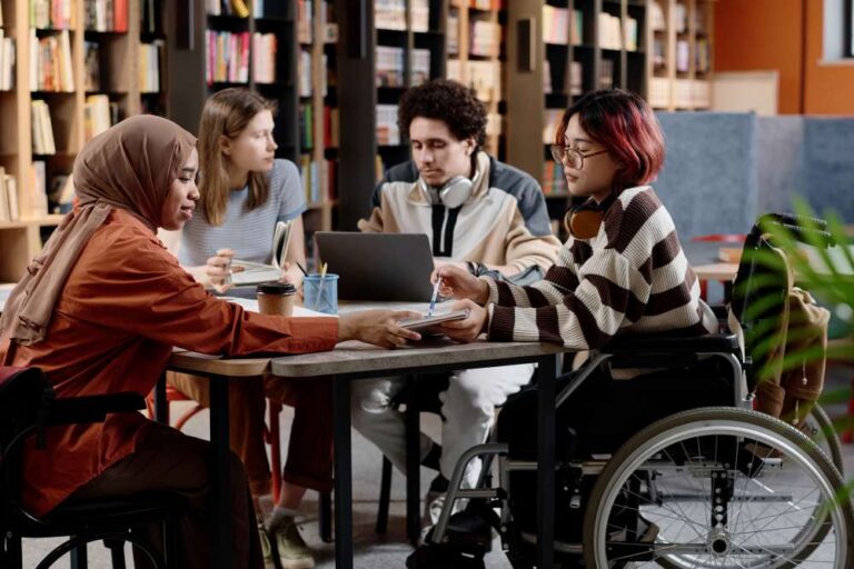 Four people gathered at a table in a library with bookshelves in the background.