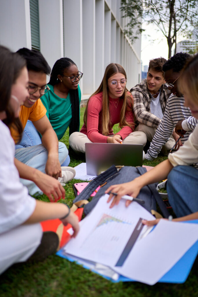 Group of young students sitting on the grass outside building