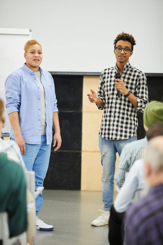 Young adult speaking into microphone while presenting together with colleague at conference